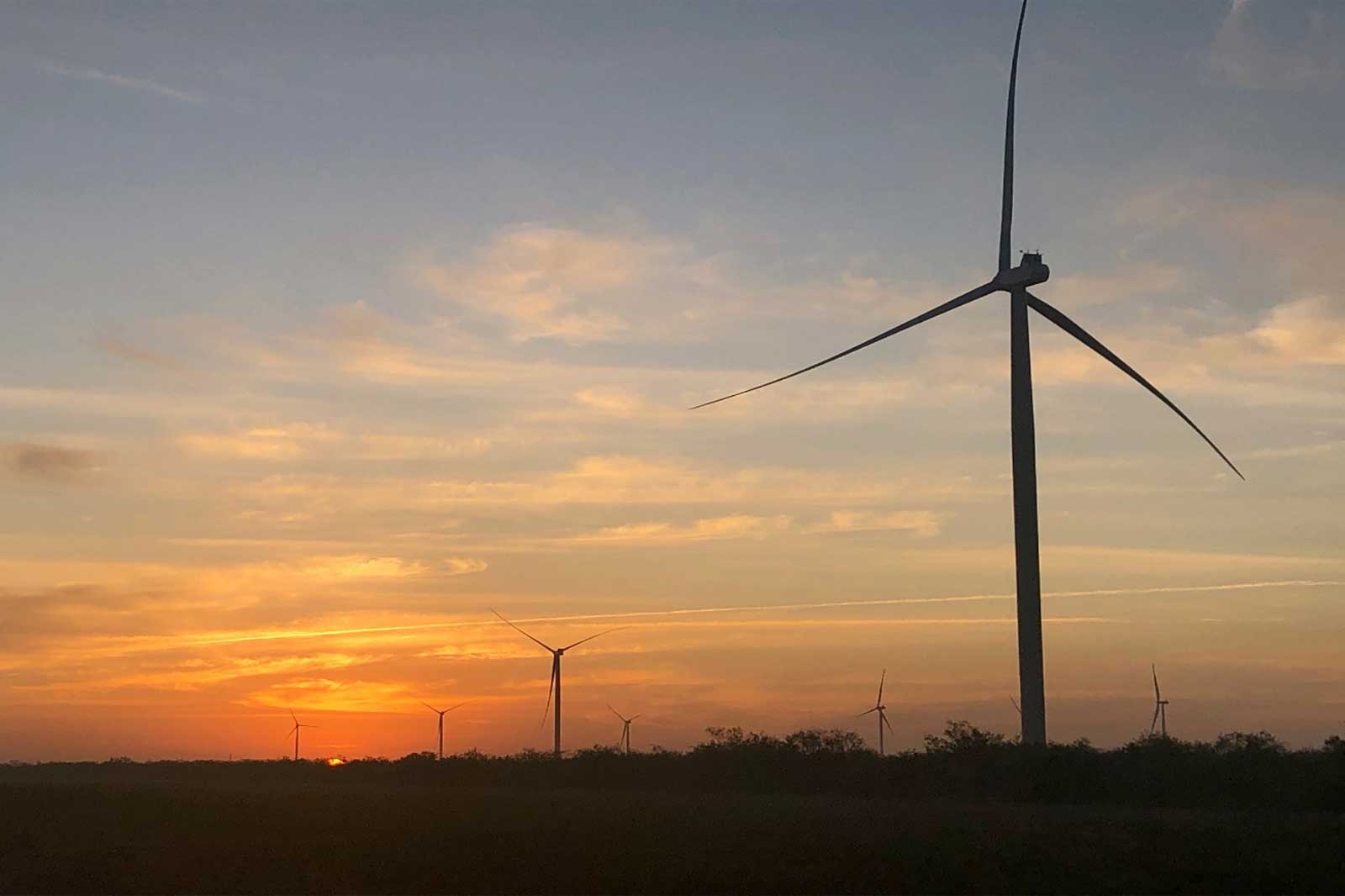 Silhouette of wind turbines against a vibrant sunset sky, featuring rich orange and purple hues.