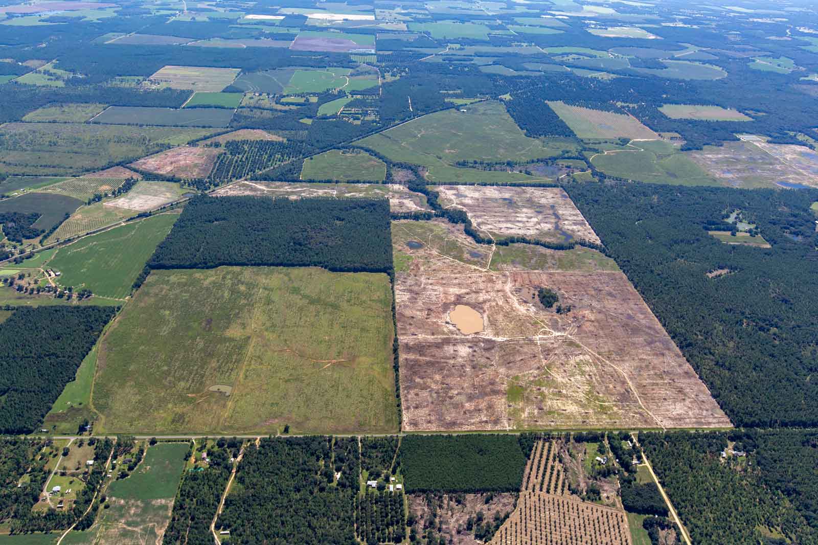 Aerial view of rural landscape featuring forests, fields, and a small water body.