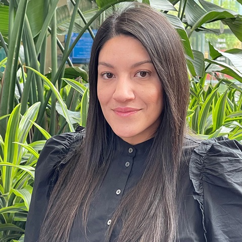 A person in a black blouse stands amongst vibrant green foliage.