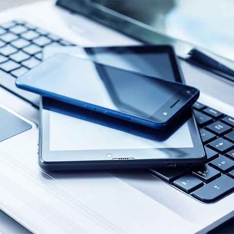 A smartphone and two tablets are stacked on top of a laptop keyboard, showcasing modern technology.