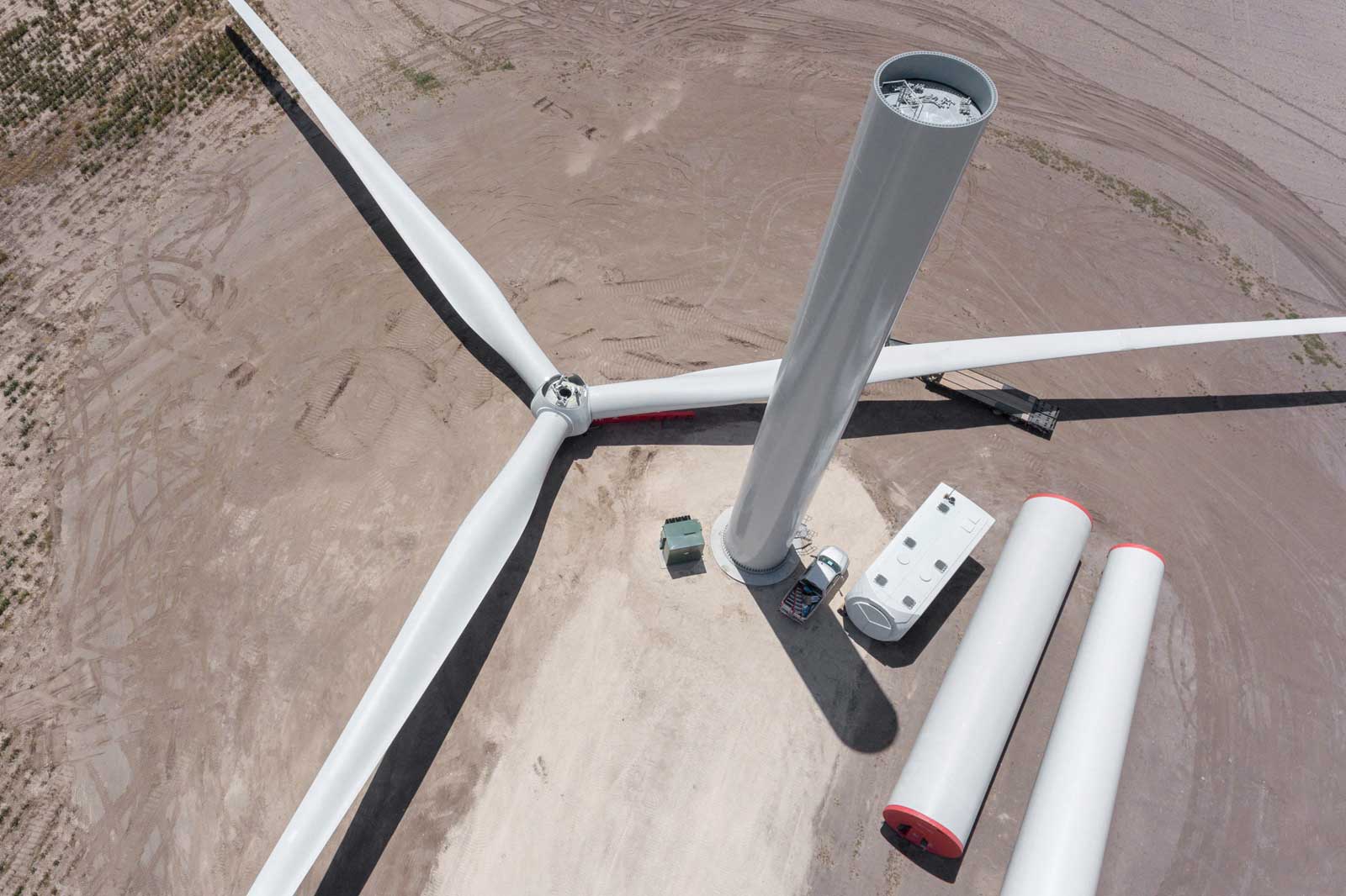Aerial view of a wind turbine with three blades, a tall tower, and nearby components on a dry landscape.