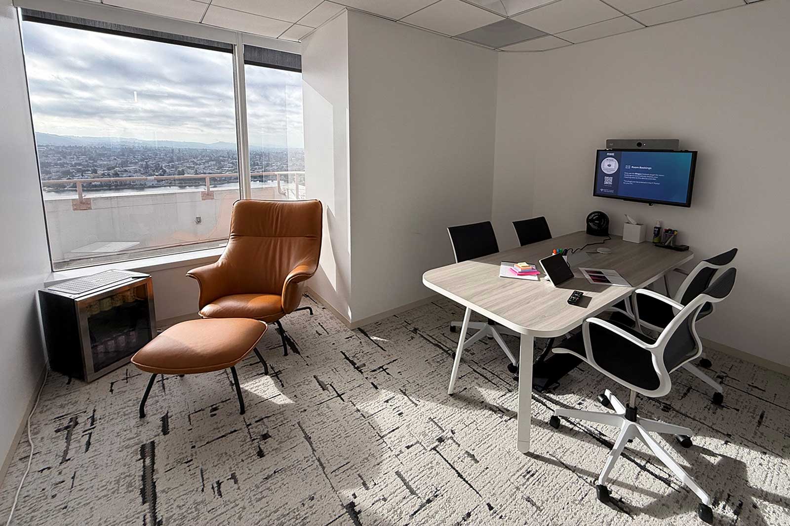 A modern office meeting room featuring a brown chair, sleek table, black chairs, and a panoramic view of the city.
