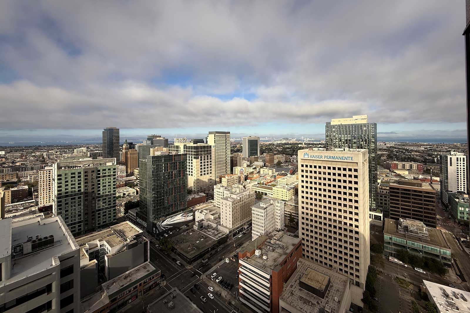 A panoramic view of a city skyline with modern buildings under a cloudy sky, showcasing urban development and distant hills.