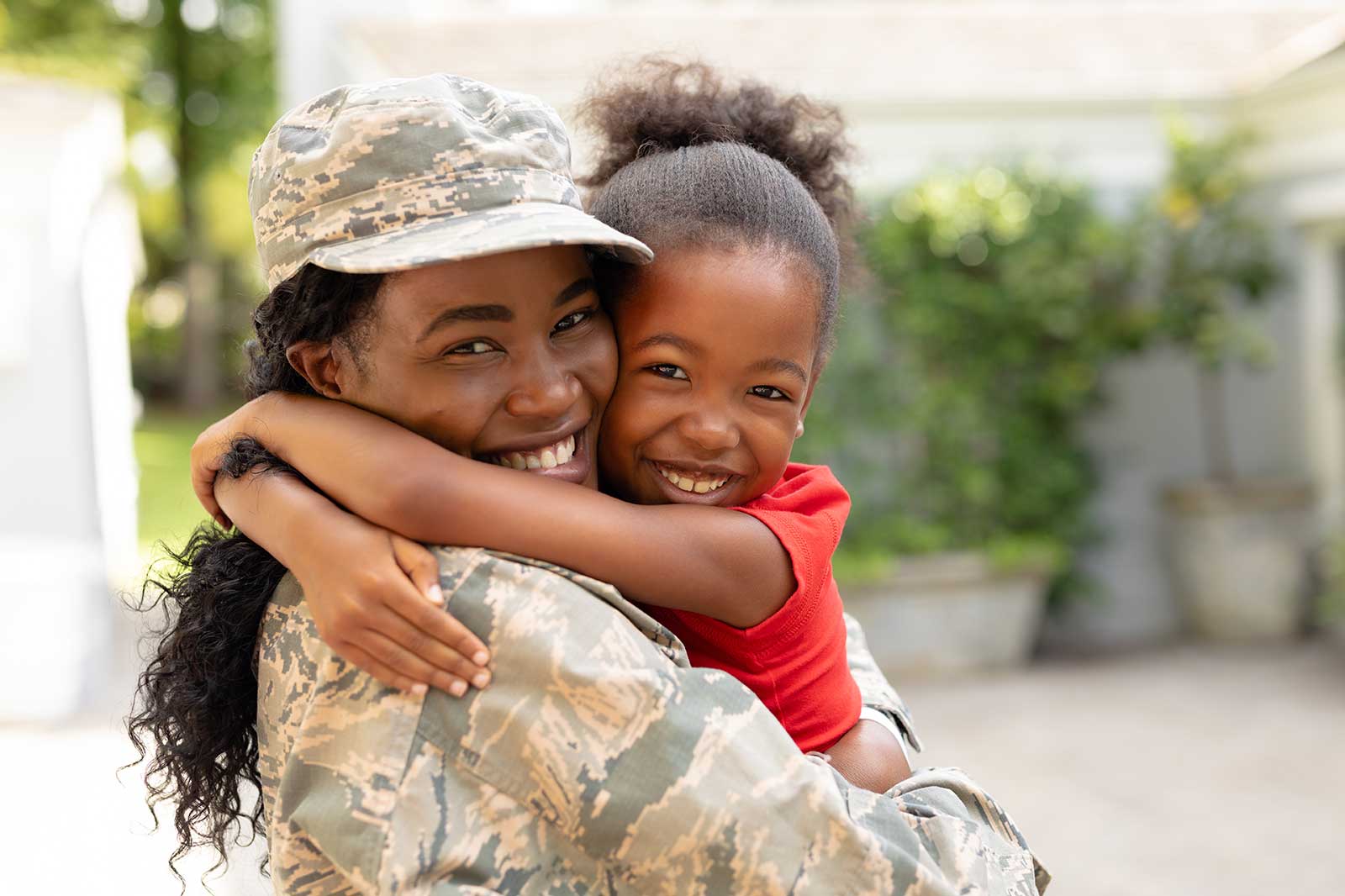 A military parent hugs a child warmly in a green outdoor setting, showcasing love and reunion.