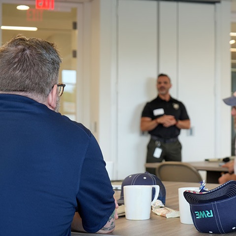 A group meeting in a modern conference room, featuring a speaker addressing an audience seated at a table.