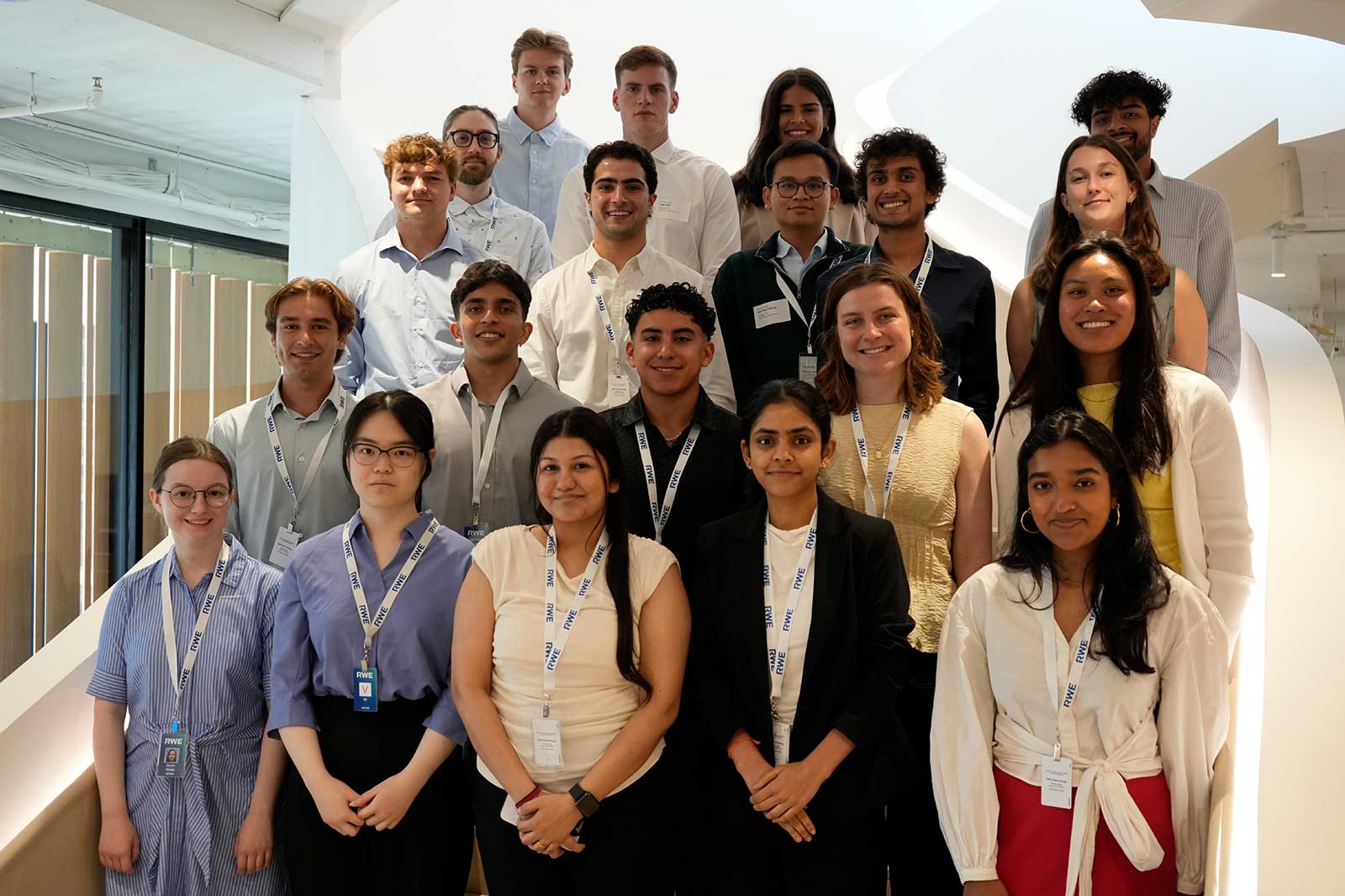 A group of individuals standing on stairs in a corporate setting, all wearing name badges around their necks.