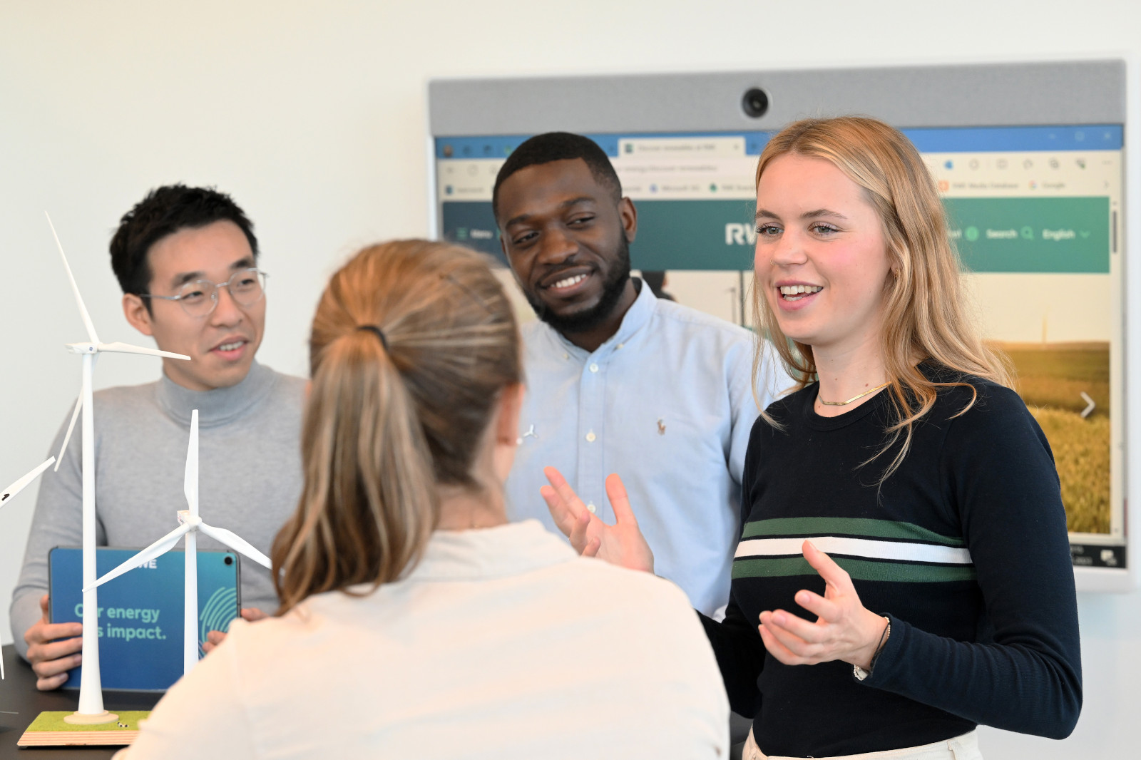 A group discussion on renewable energy featuring a wind turbine model in the foreground.