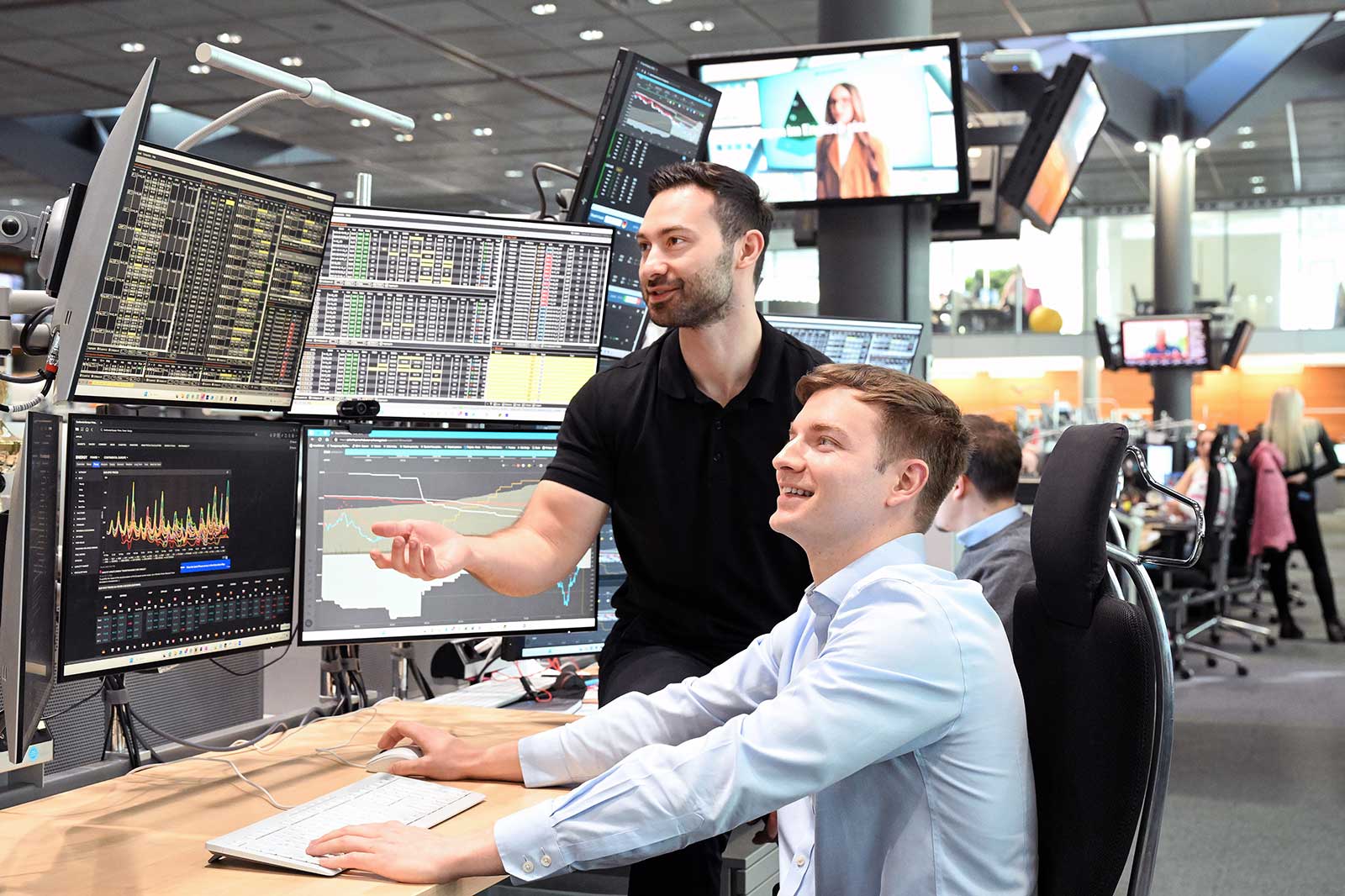 A professional trading environment with two individuals discussing data on multiple monitors, analysing financial charts.