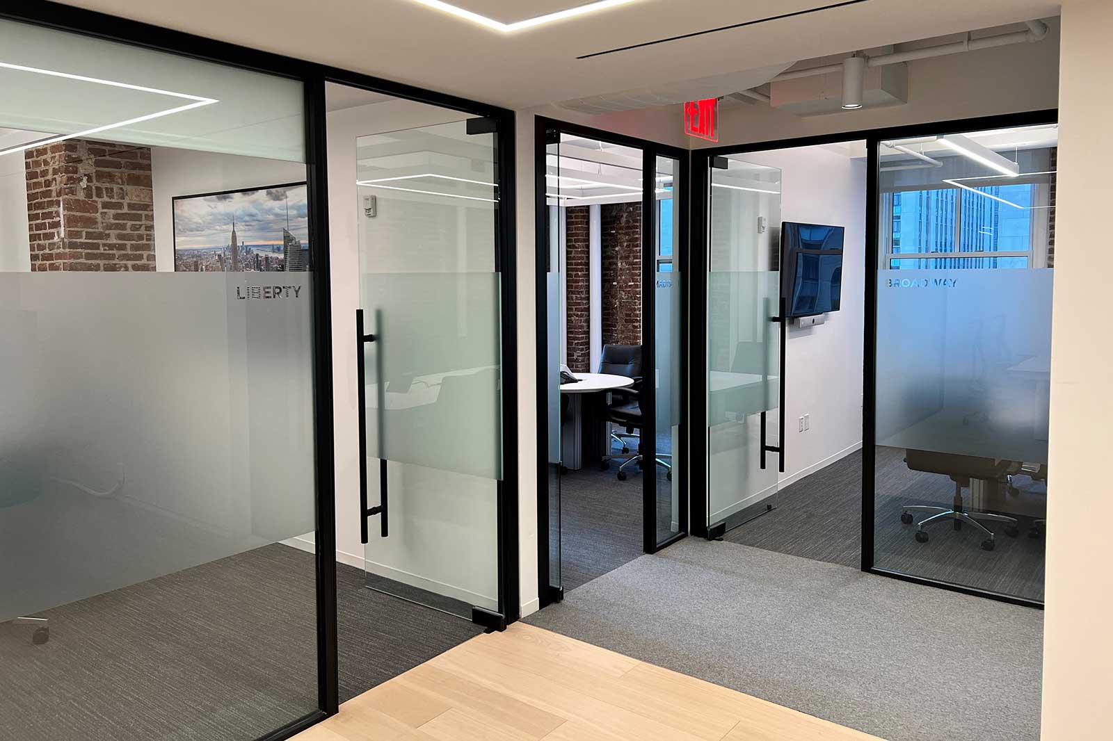 Office view with glass doors, a table and chair, and a television mounted on the wall.