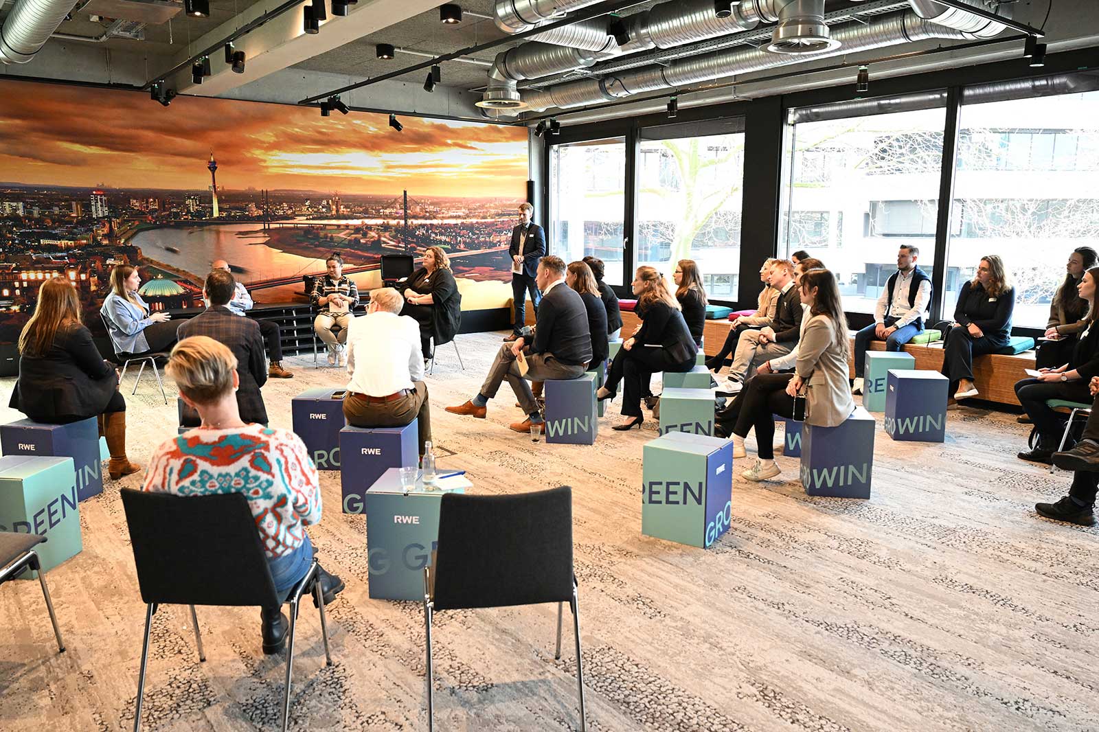 A group of four people discussing at a table with wind turbine models and digital devices in a bright office space.